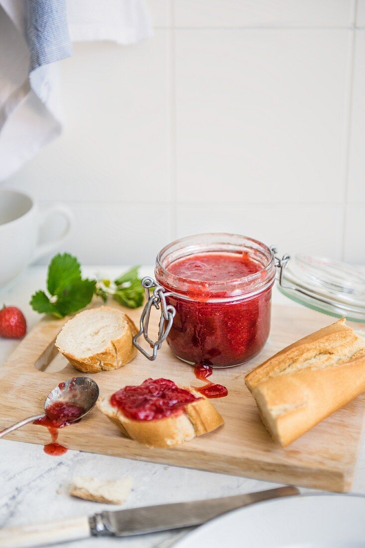 Strawberry jam in a glass jar, and spread on a slice of white bread