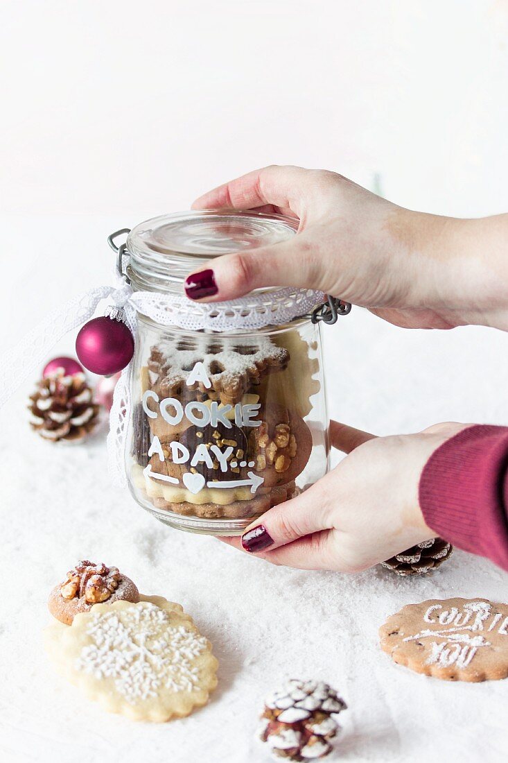 Hände halten Glas mit weihnachtlich verzierten Plätzchen