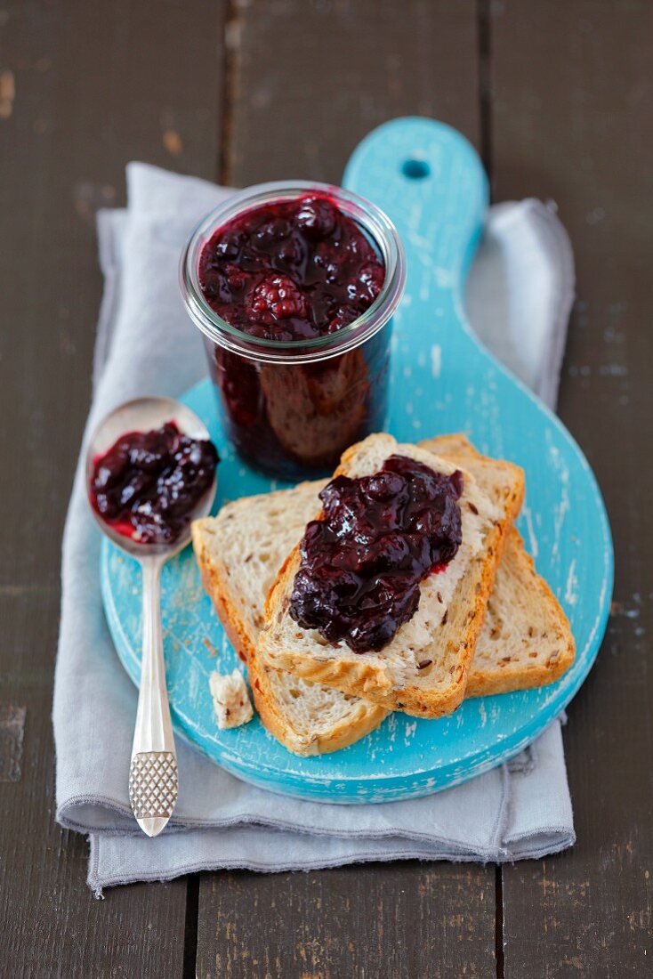 Homemade blackberry and blueberry jam in a glass and on a slice of bread
