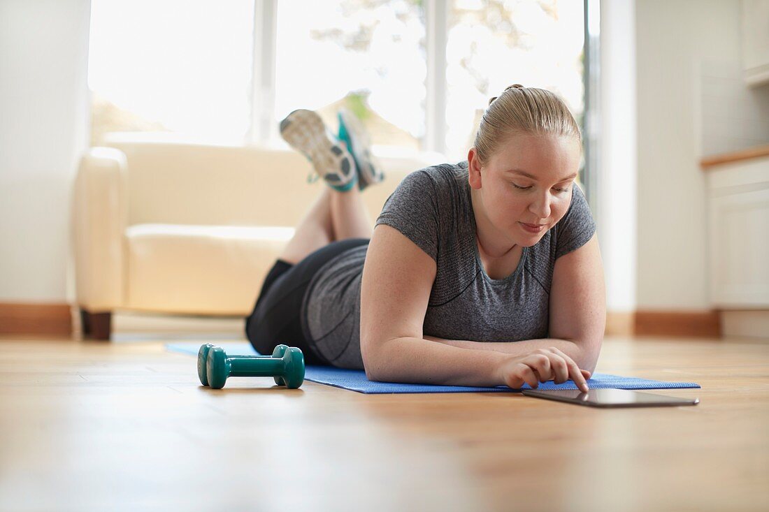 Young woman lying on yoga mat using digital tablet