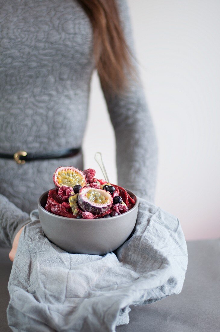 A smoothie bowl with passion fruit, raspberries, mango and blueberries