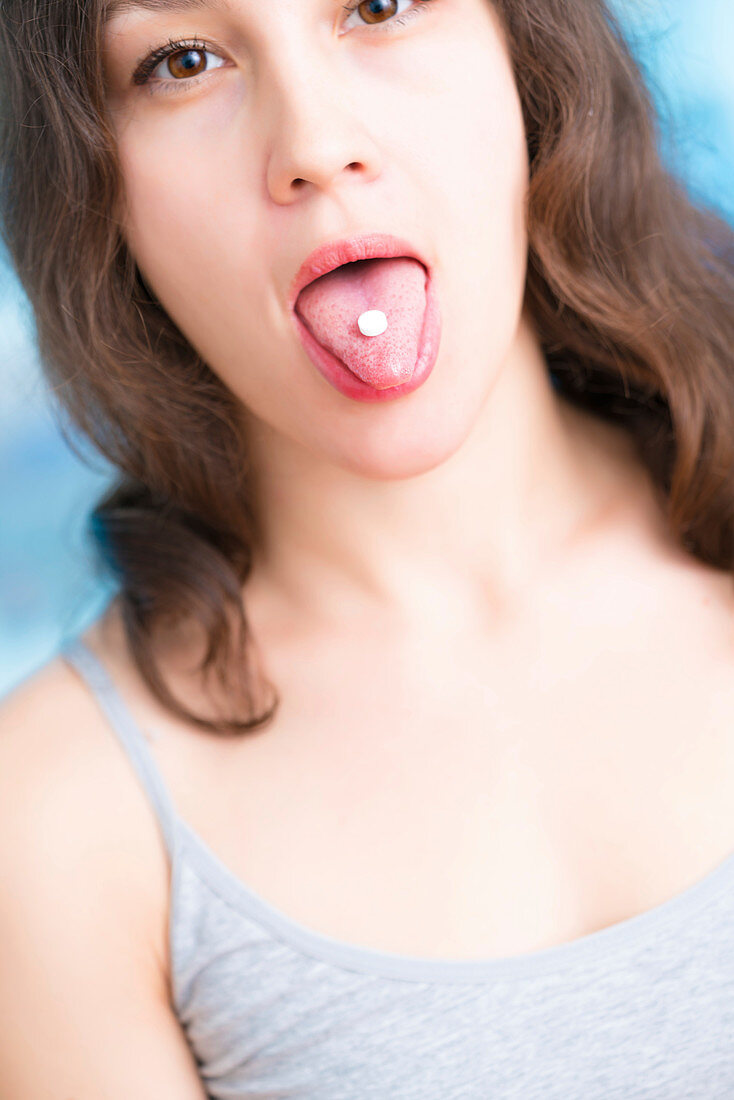 Woman with white pill on tongue