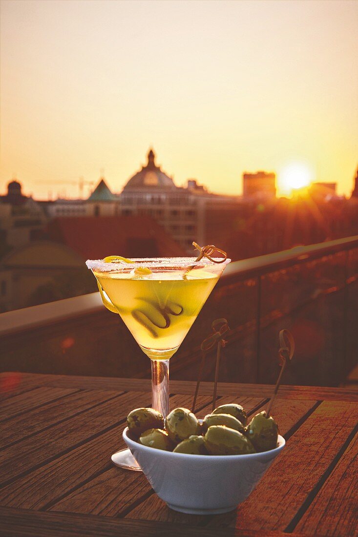 Ein Glas Martini mit Oliven in einer Rooftop Bar beim Sonnenuntergang