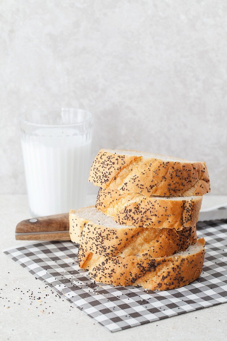 A stack of sliced poppy seed bread with a glass of coconut milk