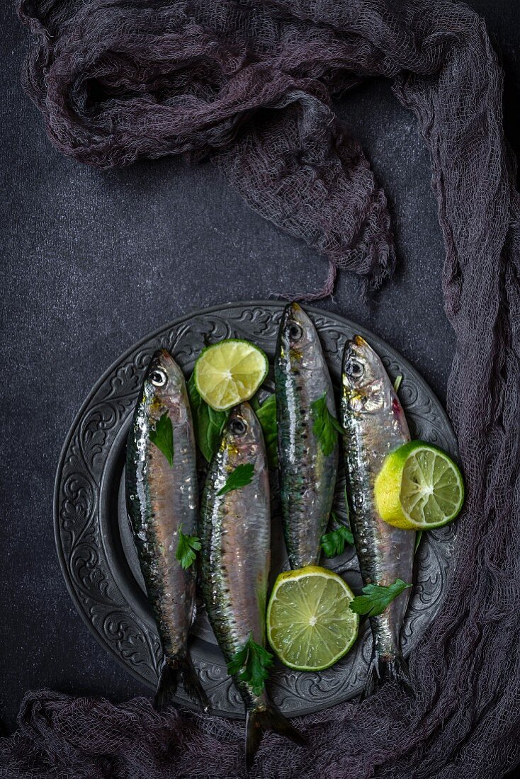 Fresh sardines with slices of lime on a metal plate (seen from above)