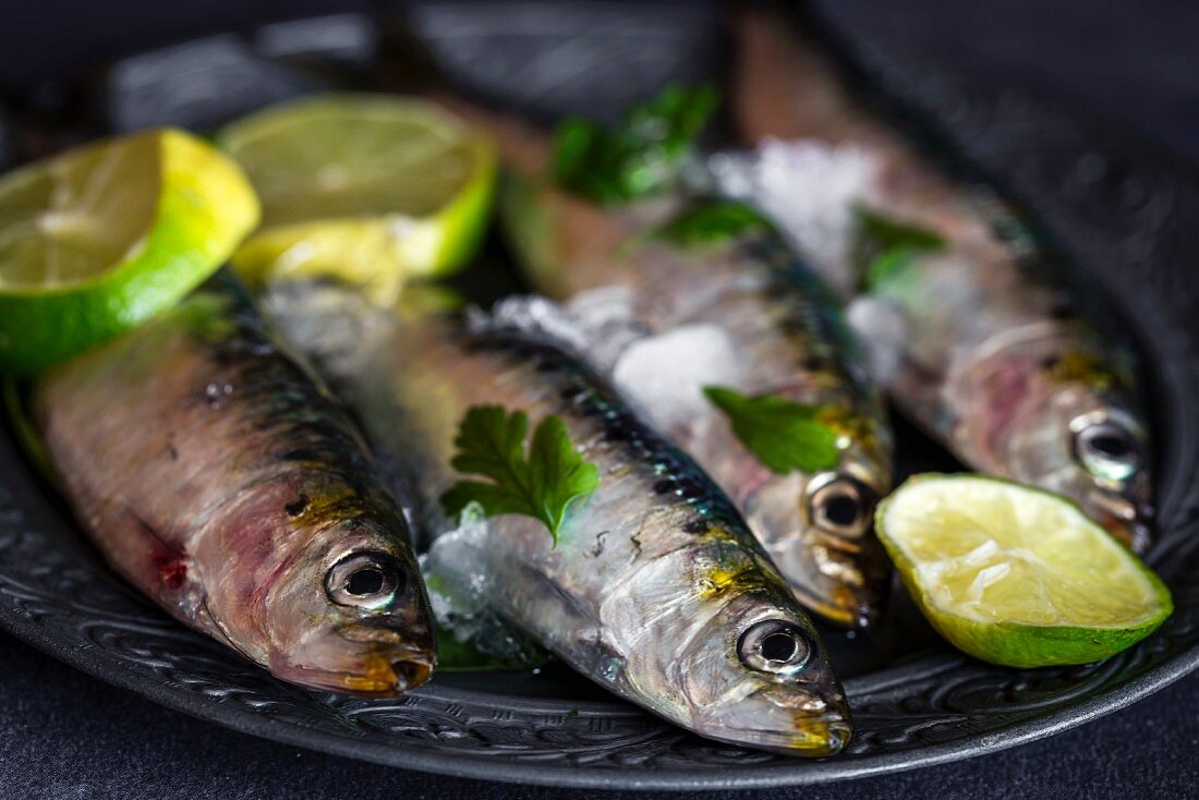 Fresh sardines with slices of lime on a metal plate (close-up)