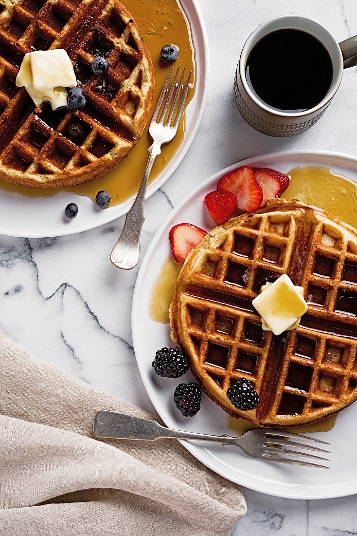 Waffeln mit Beeren, Butter und Ahornsirup zum Kaffee (Aufsicht)