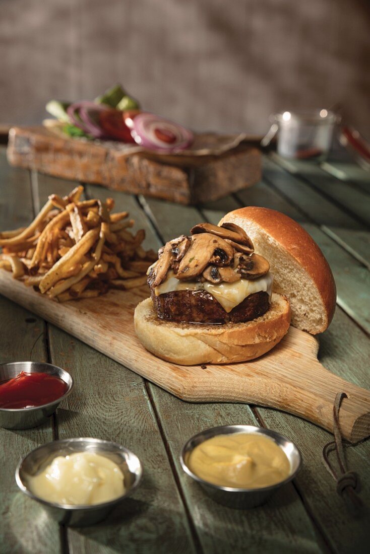 A mushroom cheeseburger with fries on a chopping board