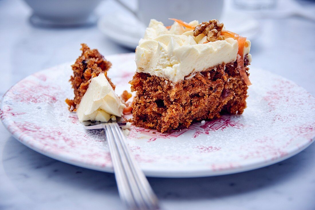 A piece of carrot cake with cream frosting on a plate