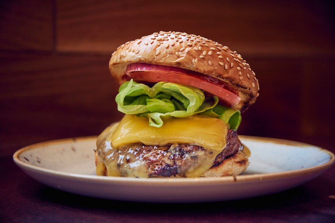 Ein Burger mit Käse, Salat und Tomate auf Teller