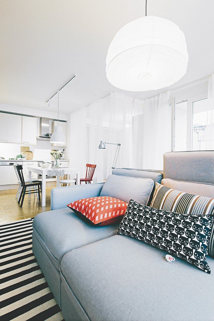 A grey sofa with cushions on a black-and-white striped rug in a light, bright open-plan living area