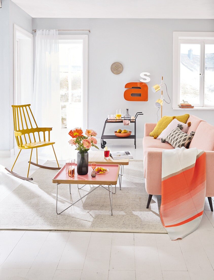 A living room with a pale pink sofa, a tray table and a yellow rocking chair