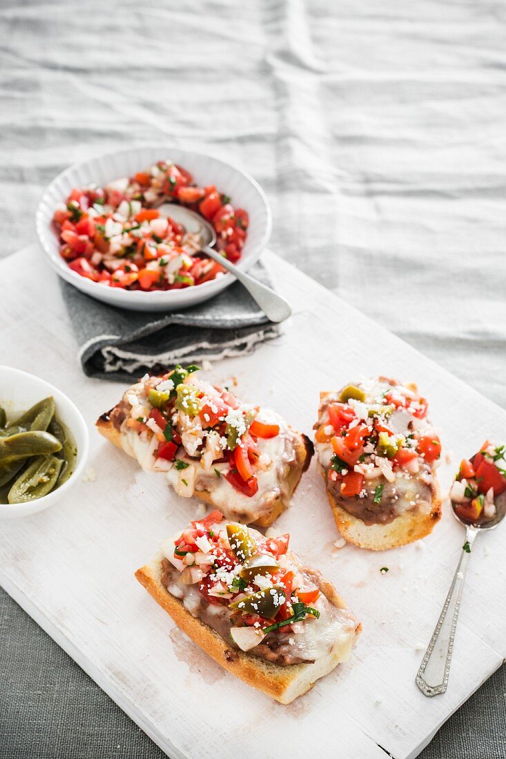 Mexican Molletes (stuffed, baked bread) with fried beans, melted cheese and pico de gallo sauce