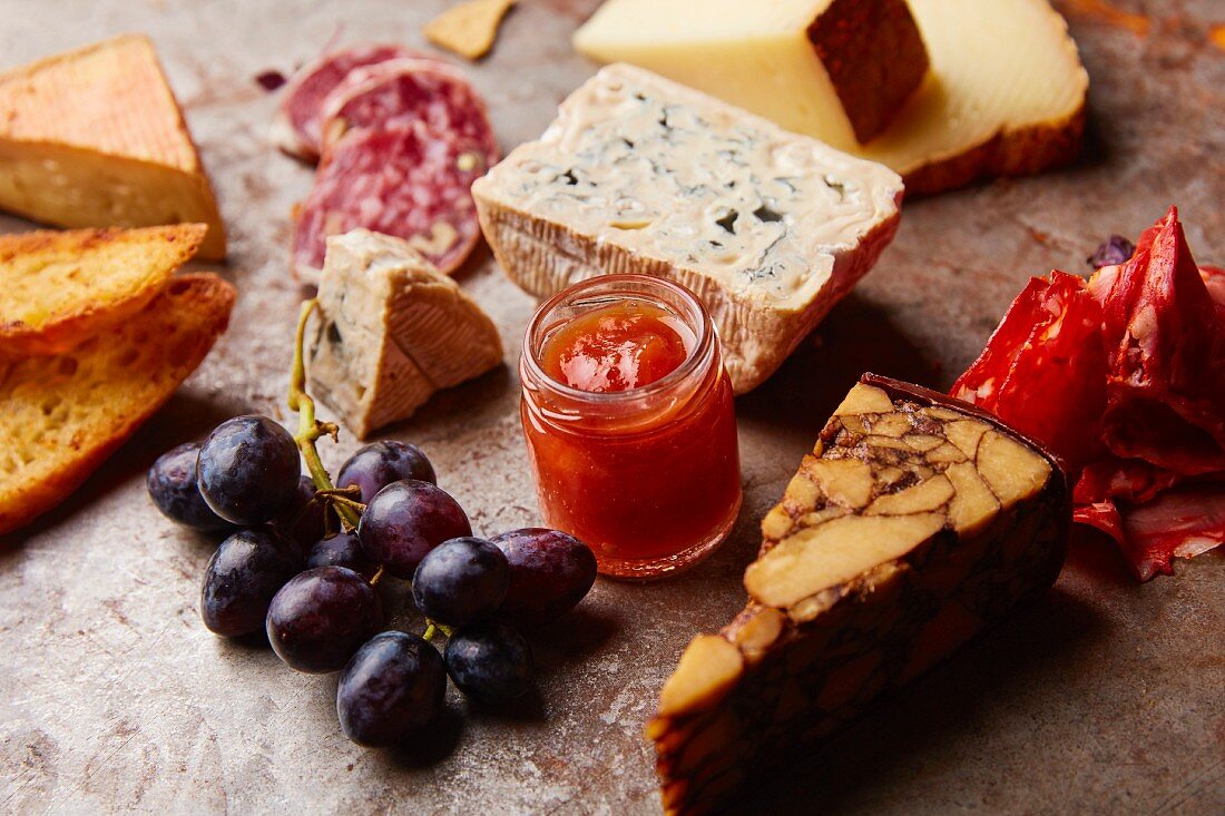 An appetizer platter with different types of cheese, salami, grapes and bread