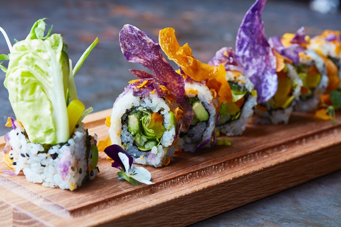 Sushi mit Gemüse- und Essblütendekoration auf Holzplatte (Japan)