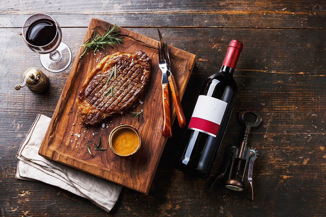 Grilled sliced Steak Rib eye with Pepper sauce and bottle of Red wine on wooden background
