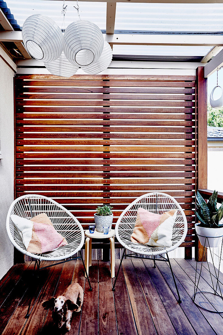 Zwei Designerstühle auf der Terrasse mit Wand aus Latten als Sichtschutz