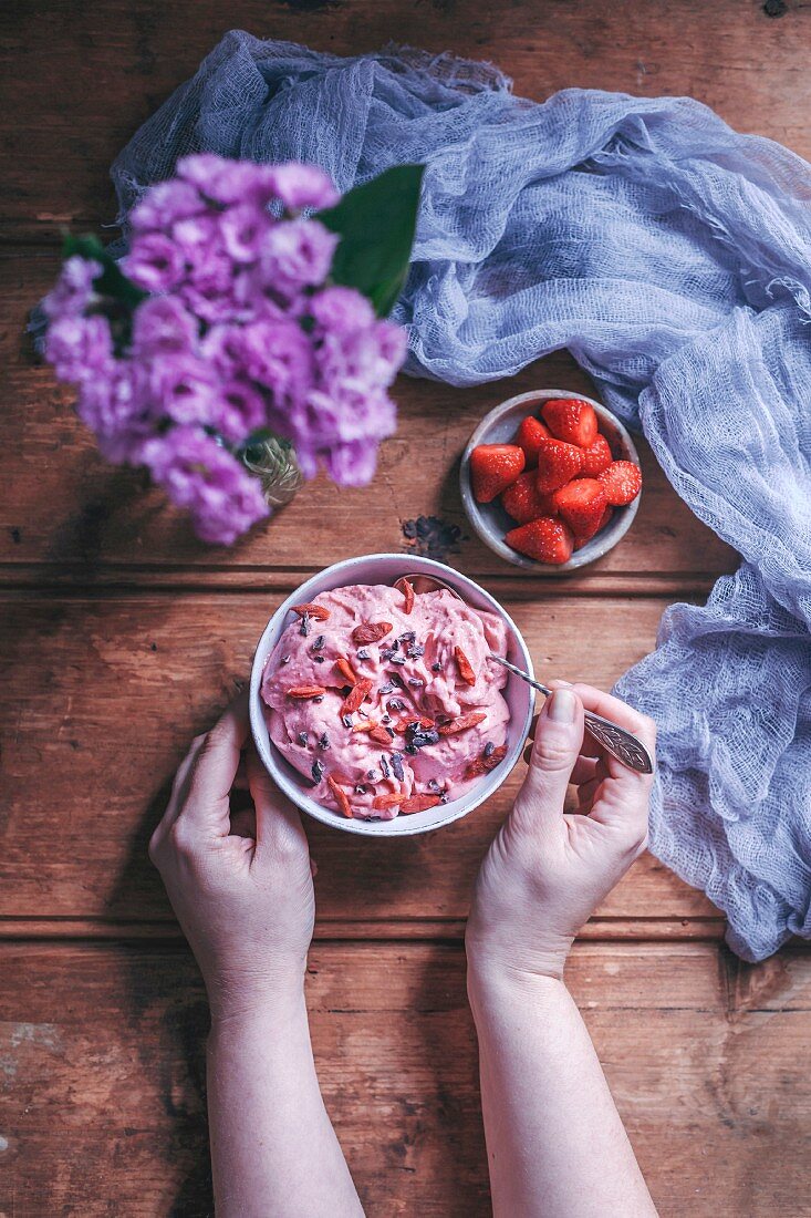 Frau isst Bananen-Erdbeereis mit Goji-Beeren und Kakaonibs