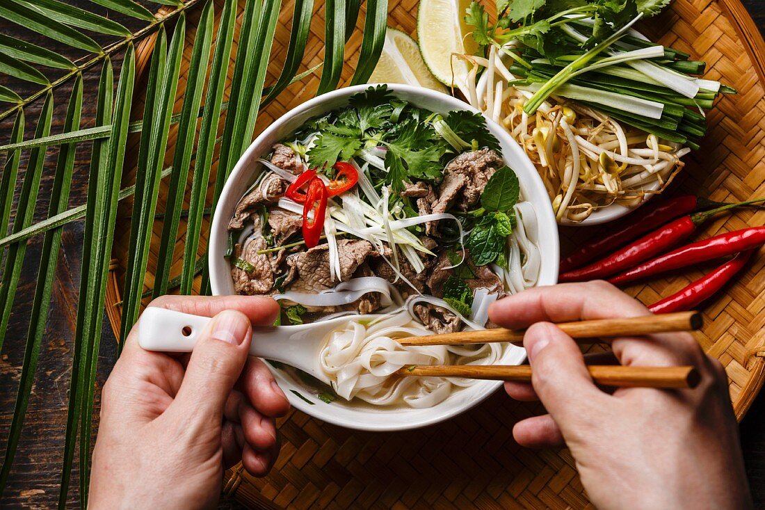 Person isst Pho Bo (Suppe mit Rindfleisch und Reisnudeln, Vietnam)