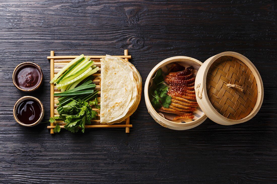 Peking Duck in bamboo steamer served with fresh cucumber, green onions, cilantro and roasted wheaten chinese pancakes