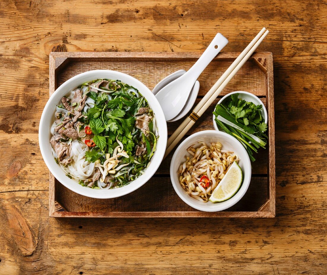 Pho Bo vietnamese Soup with beef in wooden tray on wooden background