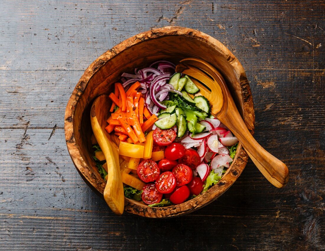Fresh vegetable salad in olive wood bowl on wooden background