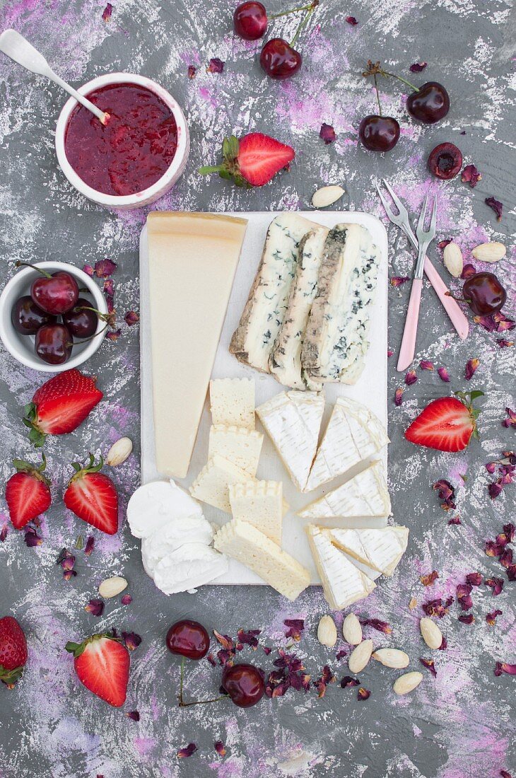 Cheese board, served with fresh fruits, strawberry jam, almonds and edible dried rose petals