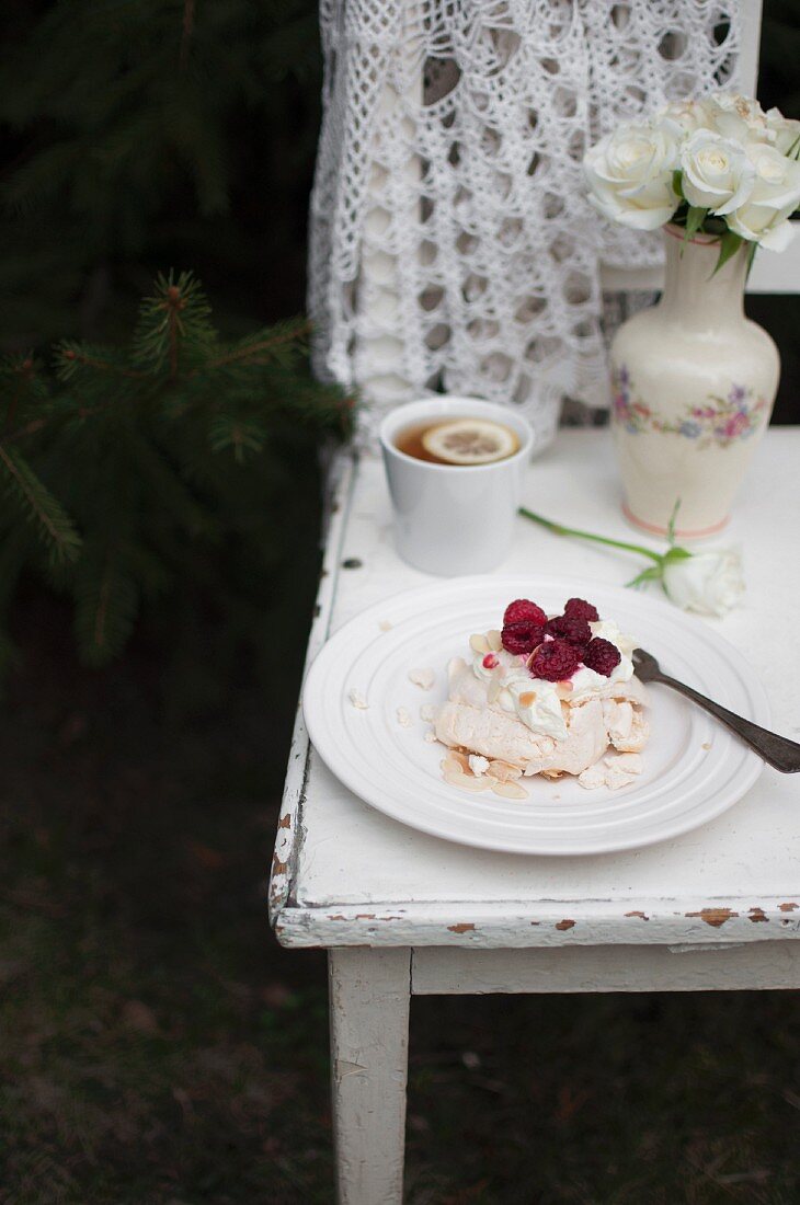 Mini Pavlova (meringue cake) with whipped cream, raspberries and almond flakes, served in the garden with cup of tea