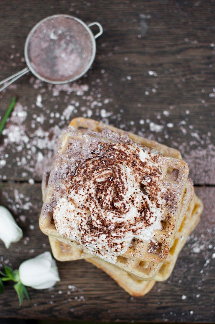 Waffles served with whipped cream, sprinkled icing sugar with cocoa powder