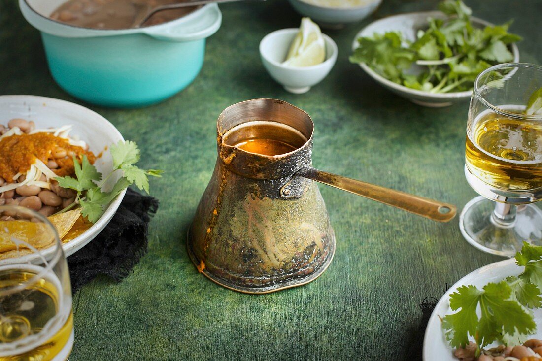 Ranchero Sauce in a vintage copper ladle on a green background