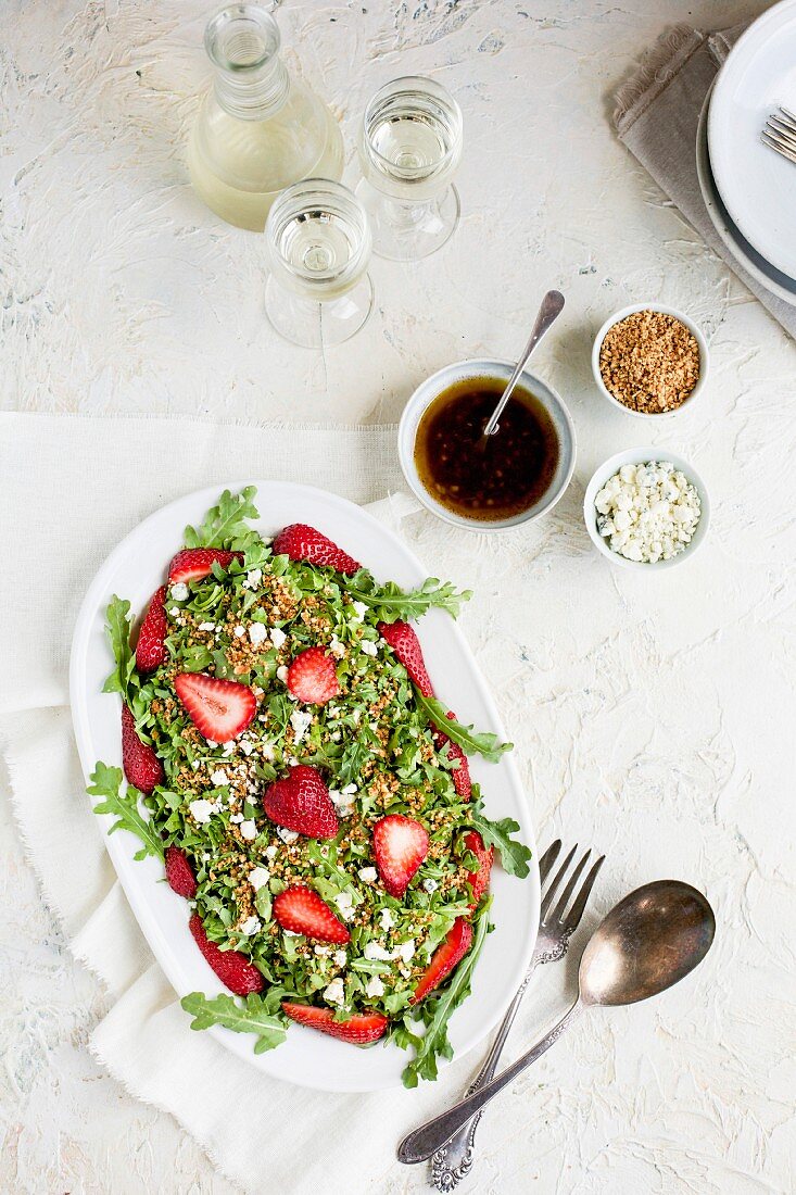 Strawberry Arugula Salad with Hibiscus Vinaigrette served with white wine on a white plaster background