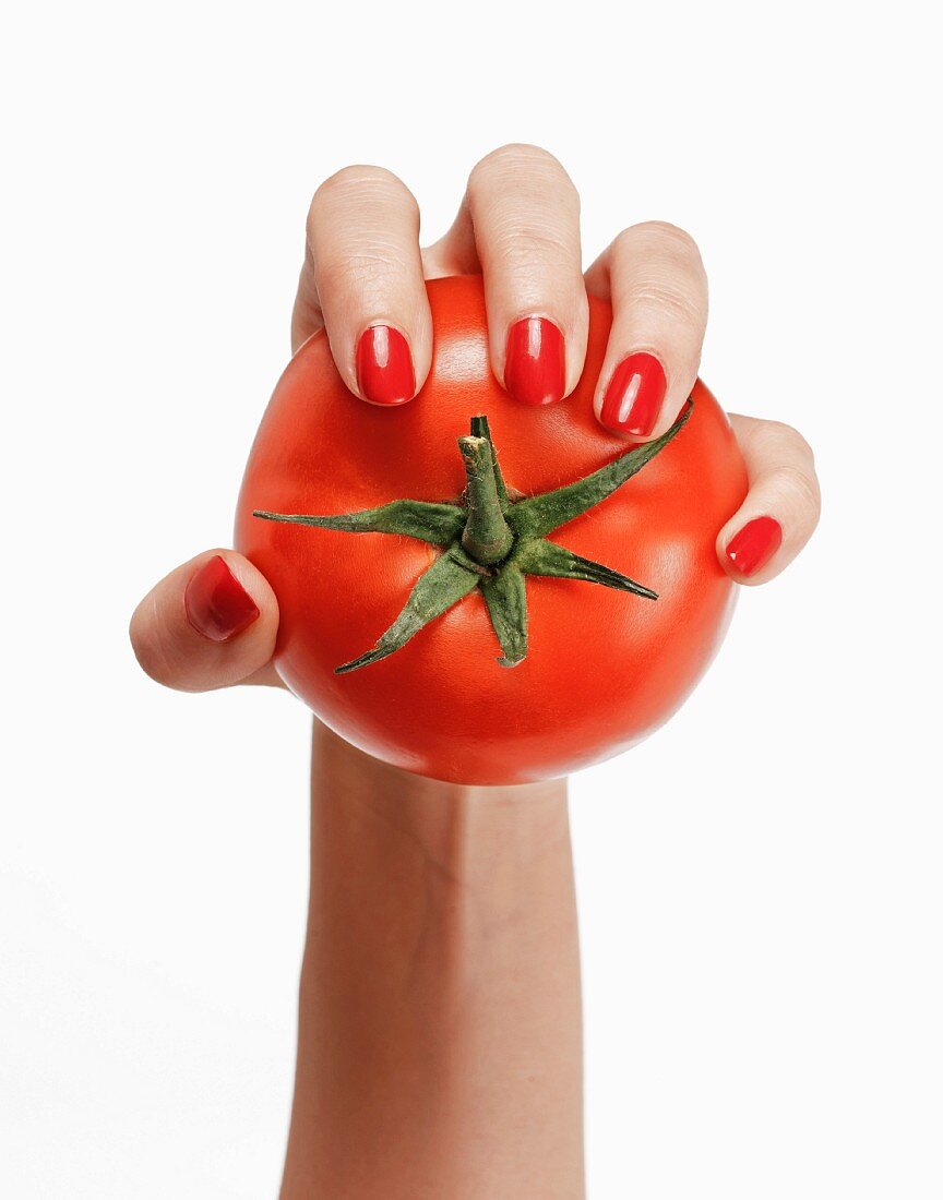 A woman's hand with red fingernails holding a tomato