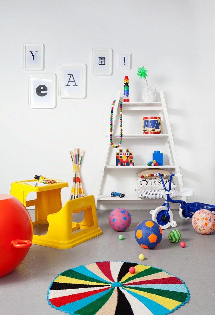 Yellow plastic desk and bench, colourful toys, blue tricycle and white shelves in child's bedroom