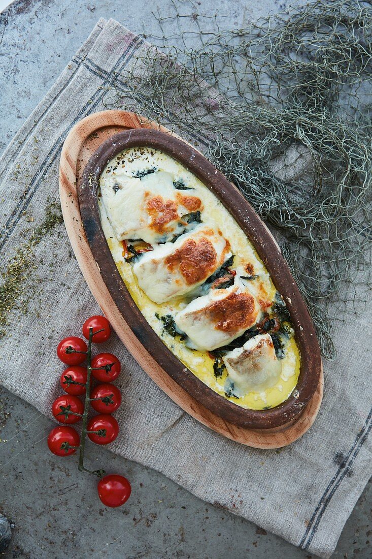 Cheese topped fish with spinach and tomatoes in cream sauce (top view)