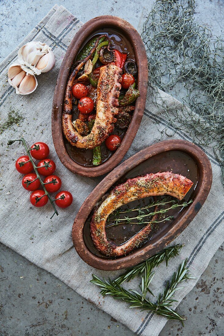 Octopus tentacles with tomatoes, peppers and herbs in rustic serving dishes