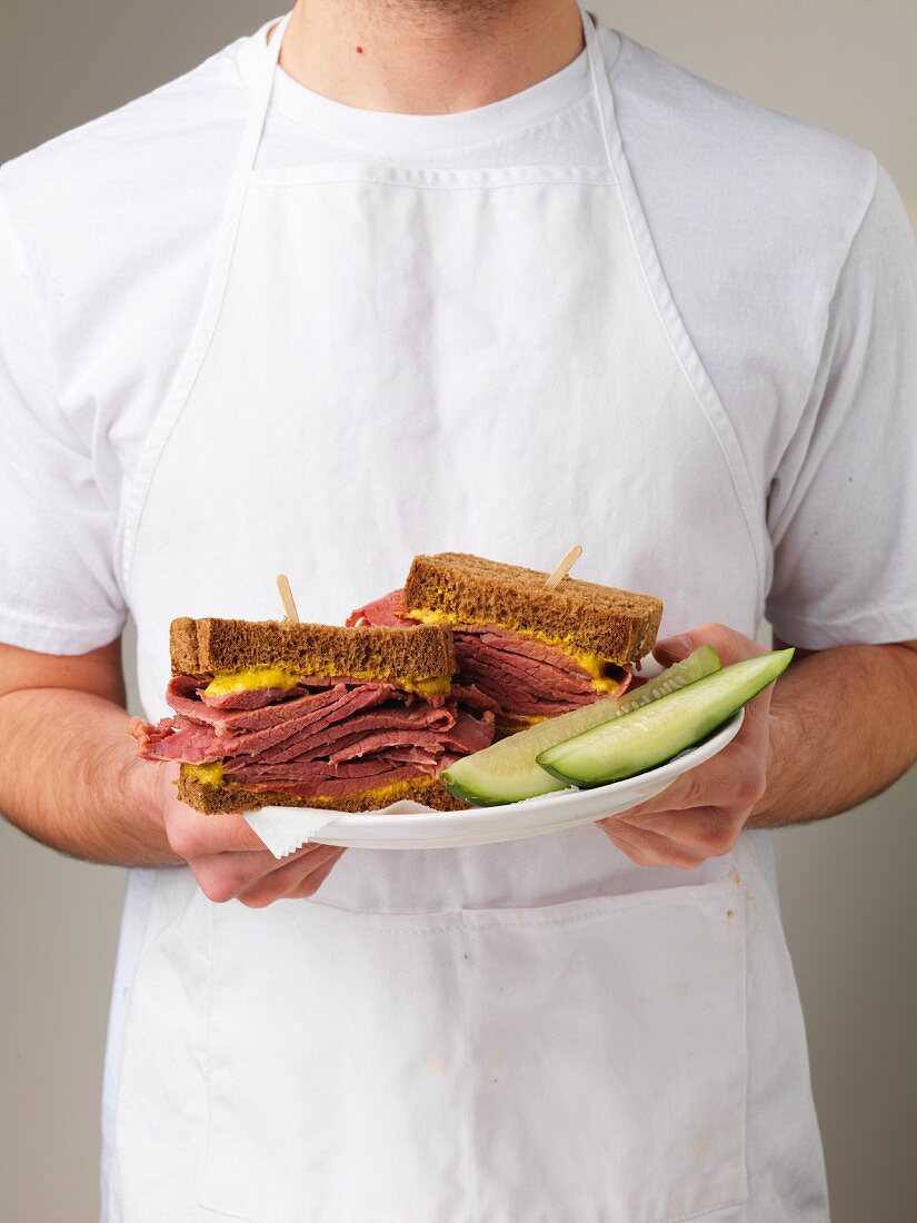 Mann hält Teller mit Corned Beef Sandwiches