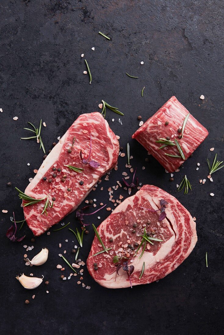 Various beef steaks with herbs and spices on a black background