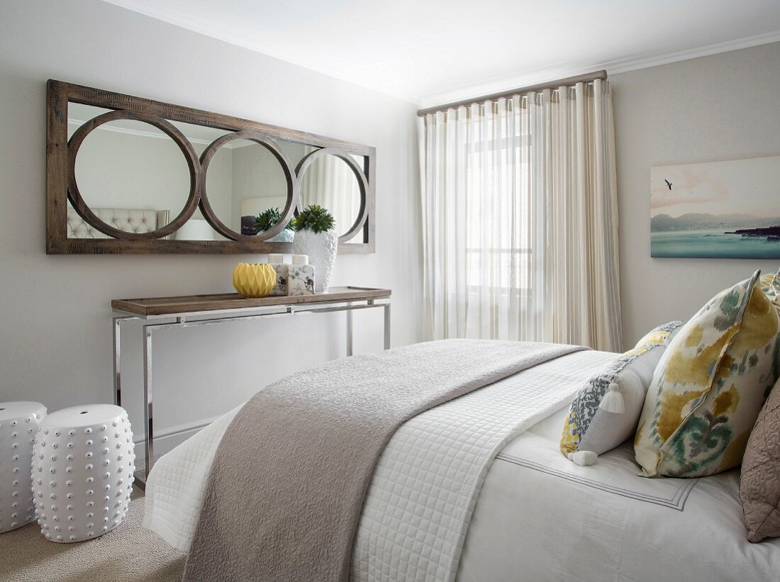 Holzrahmenspiegel über Konsolentisch und weiße Keramikhocker im Schlafzimmer mit Doppelbett
