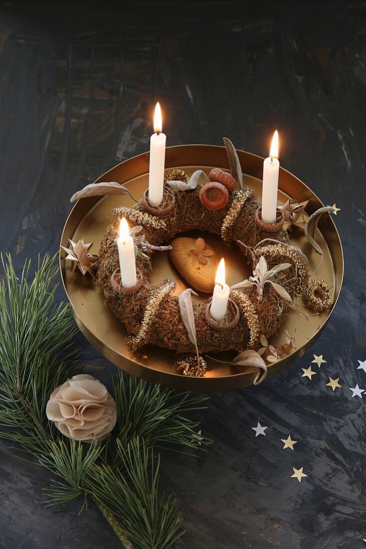 A homemade advent wreath with burning candles on a golden cake stand