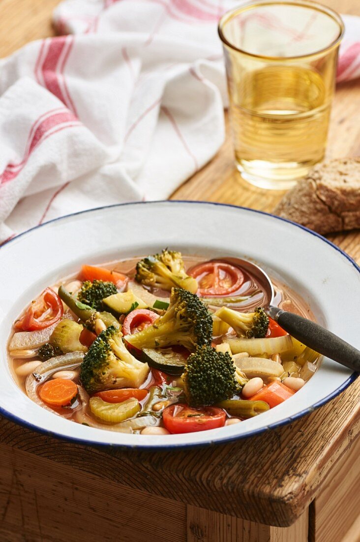 Minestrone in an enamel plate on a rustic wooden table