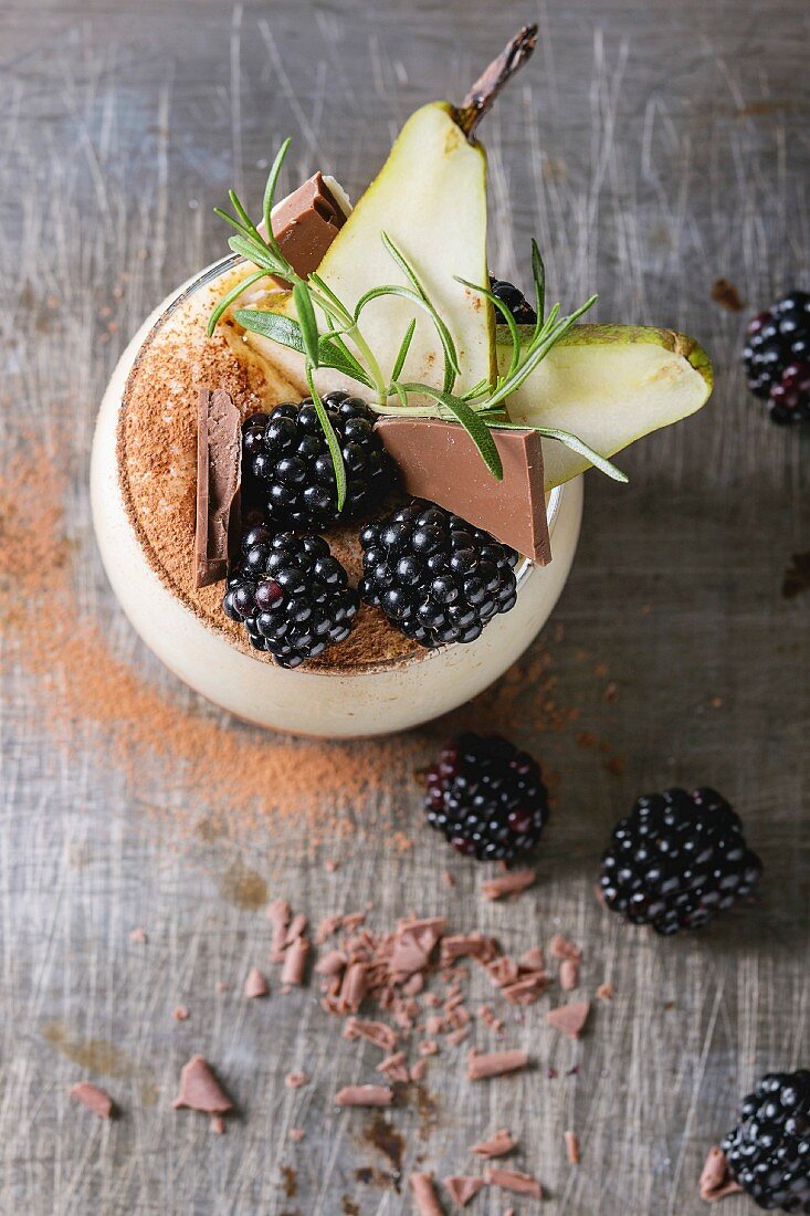 Dessert breakfast layered chia seeds, chocolate pudding, rice porridge in glass decorated by fresh blackberries, sliced pear, cocoa powder