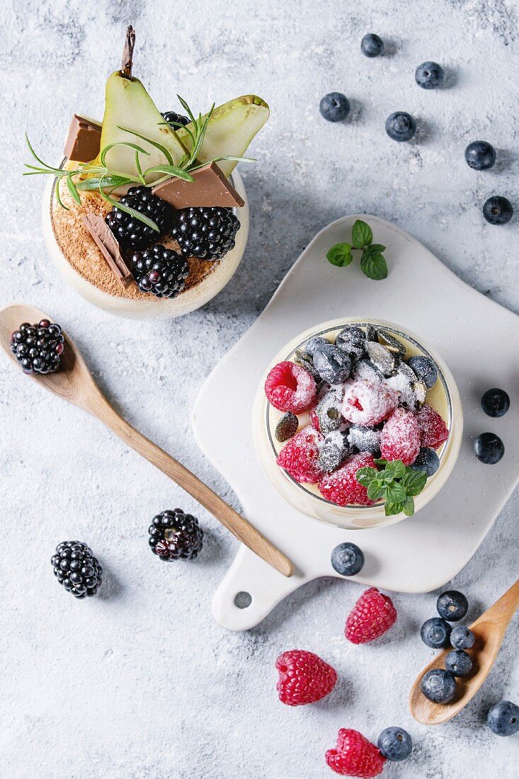 Various dessert breakfast layered chia seeds, chocolate pudding, rice porridge in glass decorated by fresh blackberries, sliced pear, cocoa powder