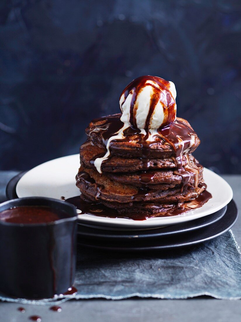 A tower of chocolate pancakes with vanilla ice cream and fudge sauce