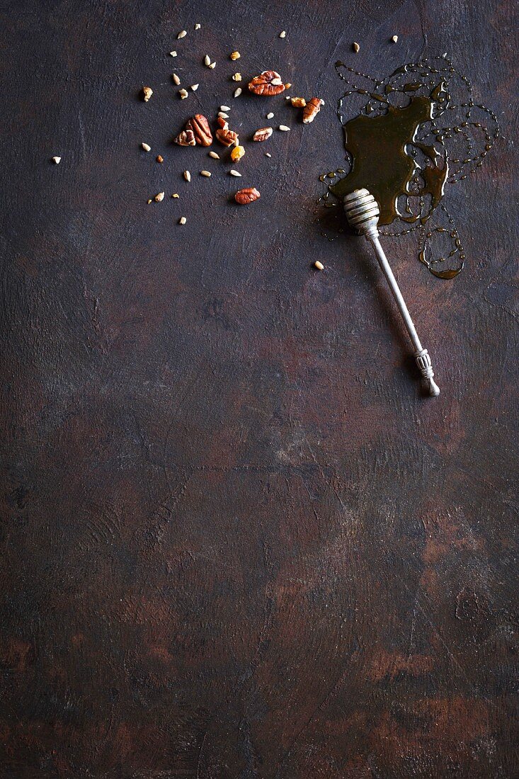 A honey dipper and various nuts on a dark background