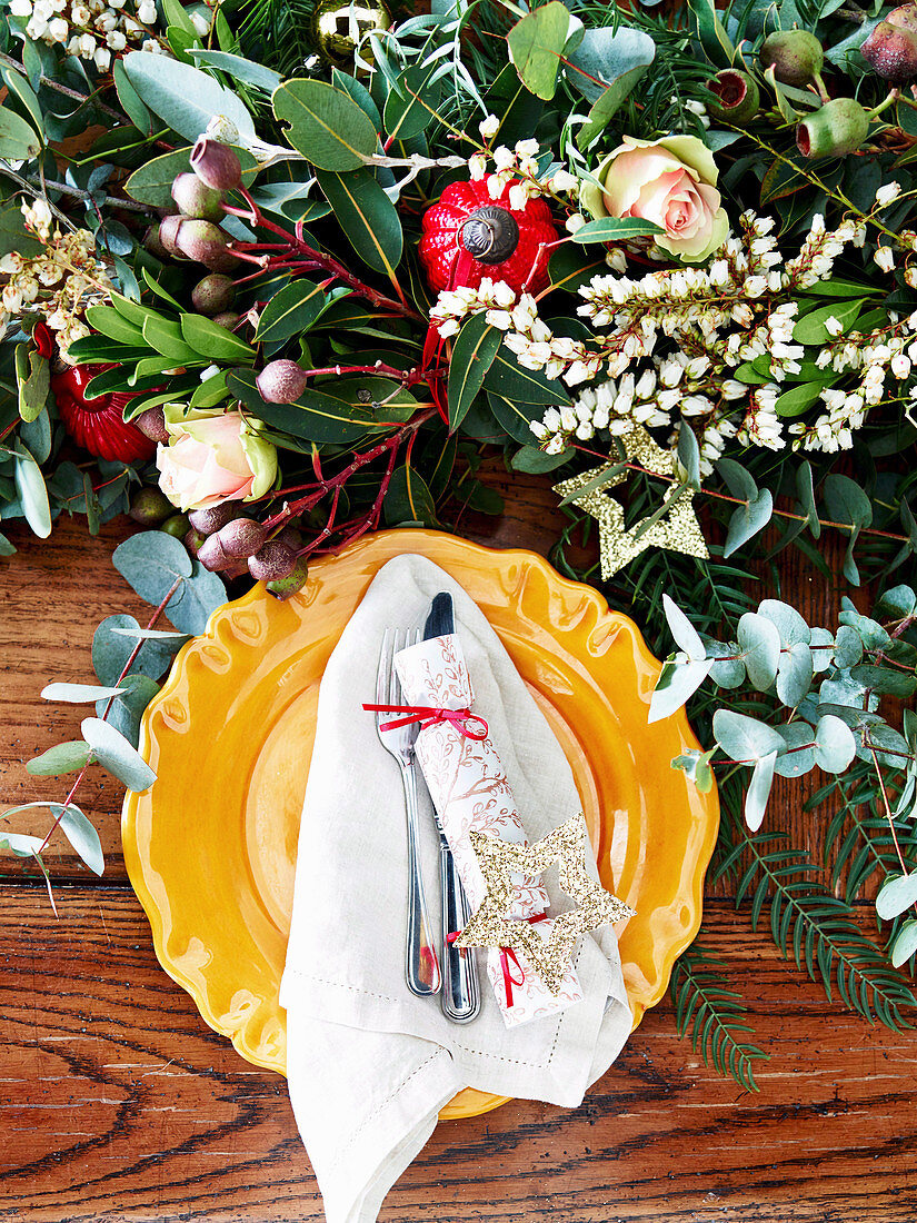 Place setting with yellow plate and festive flower decoration on table