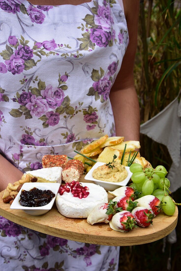 A woman holding a cheese plate with fruit, houmous, and bruschetta