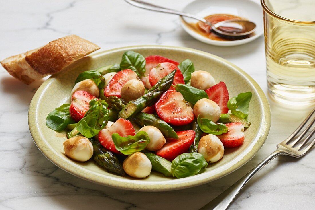 A salad with green asparagus, strawberries, mini mozzarella balls and fresh basil