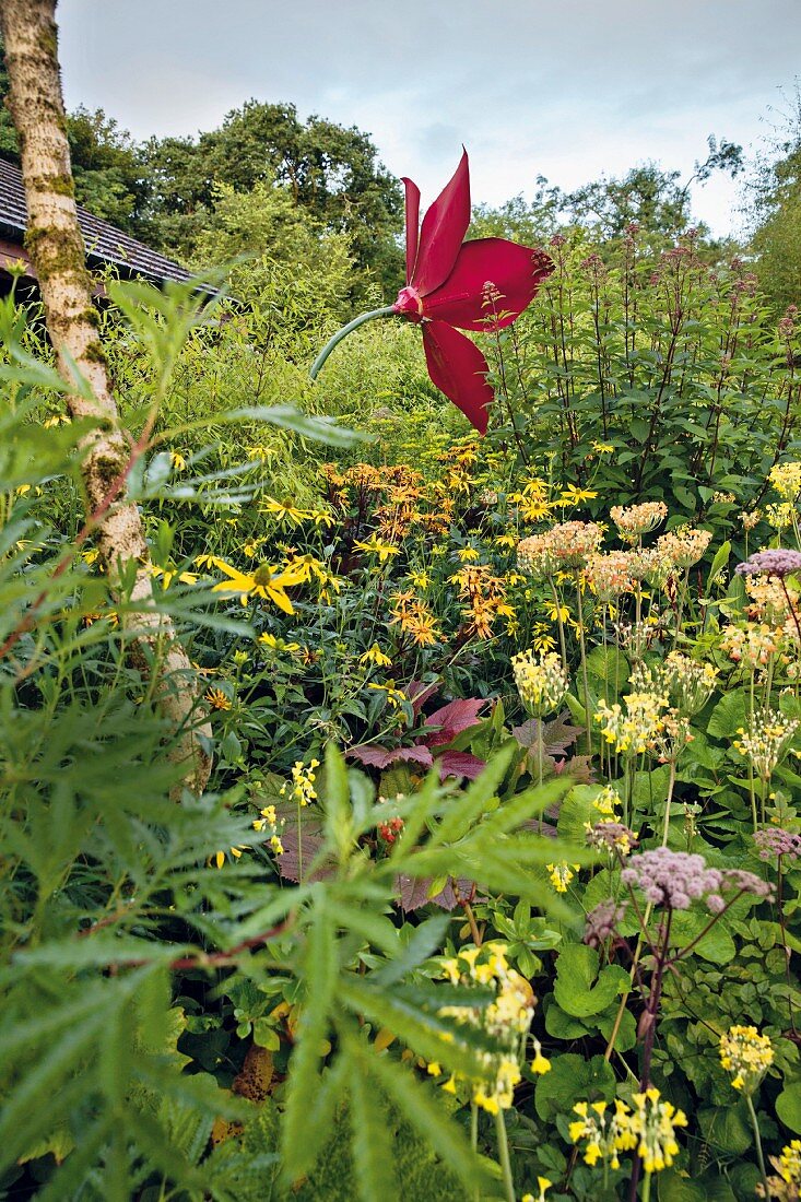 An artificial red flower, Tibetan primroses, Ligularia 'Britt Marie Crawford' and red-stemmed Eupatorium in a garden in Blessington, Ireland