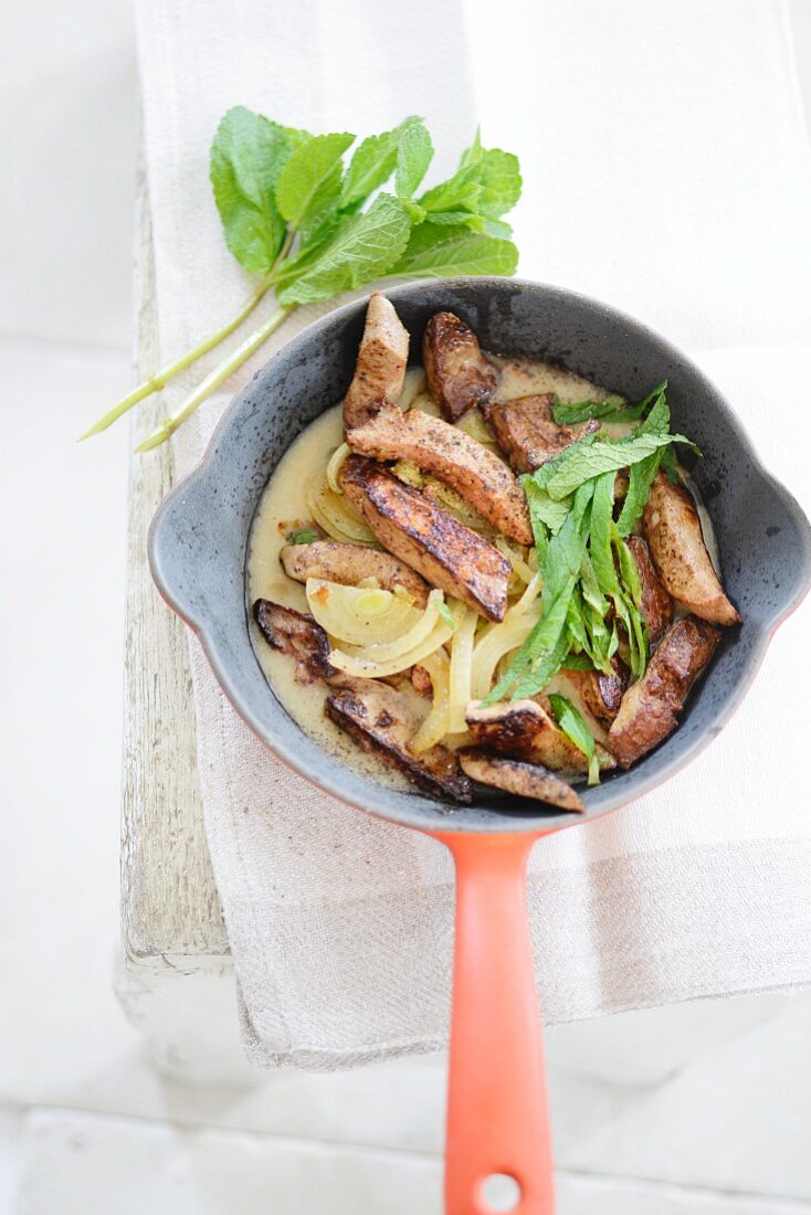 Fried liver with onions and mint in a frying pan