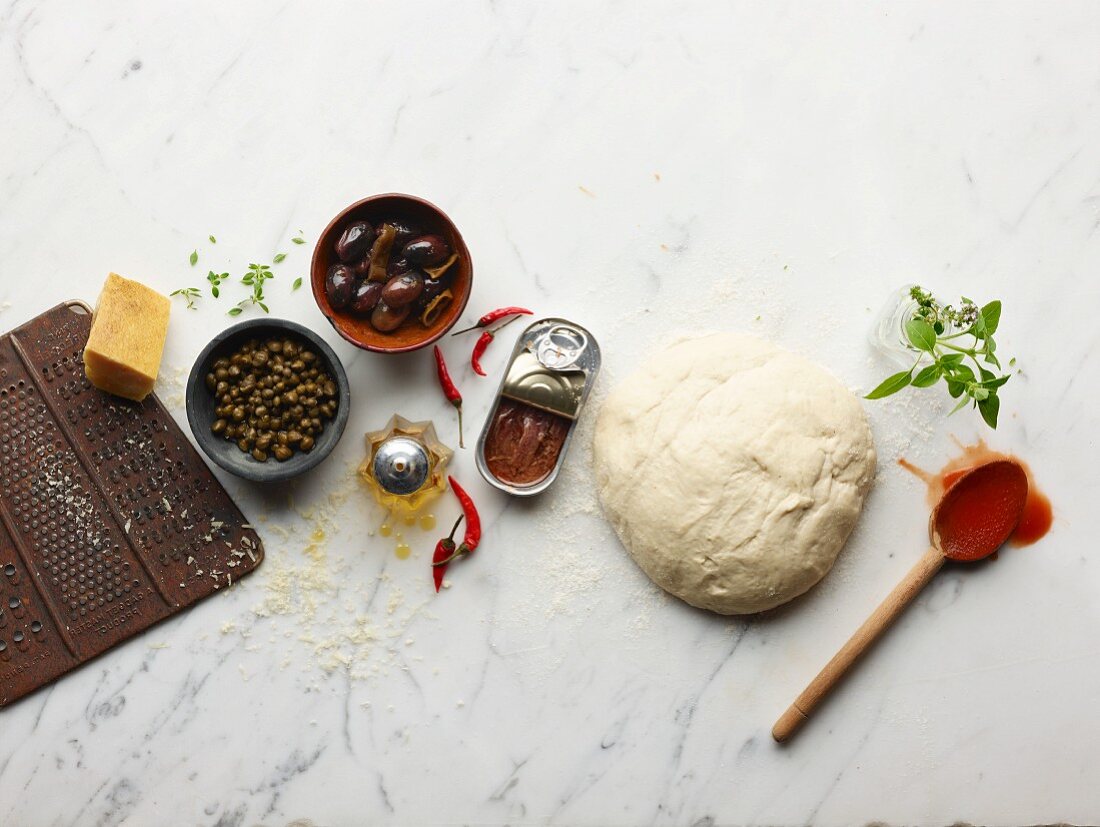 Ingredients for making pizza: pizza dough, anchovies, capers, olives, parmesan